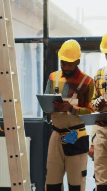 Vertical video: Team of men checking supplies and cargo in depot, using laptop and inventory list in storage room. Workers organizing stock with cardboard boxes on shelves, check merchandise in