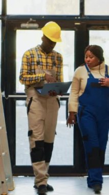 Dikey video: Afro-Amerikalı insanlar envanter çıkarmak için dizüstü bilgisayar kullanıyorlar, raflardaki karton paketlere bakıyorlar. Depoda çalışan erkek ve kadın stok ve ürünleri kontrol ediyor..