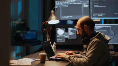 Genç erkek geliştirici gece geç saatlerde dizüstü bilgisayarda kodlama dili kullanarak birden fazla ekranda sunucu kodu yazıyor. Yeni html betiği geliştirmek için monitörlere çevrimiçi güvenlik duvarı sistemi programlanıyor.