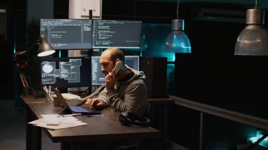 Erkek uygulama geliştiricisi gece geç saatlerde ev telefonuna cevap veriyor, telefon kablosuyla konuşuyor ve kaynak kodunu yazıyor. Ajans için algoritma oluşturuluyor, Html betiği yazılıyor. El kamerasıyla..