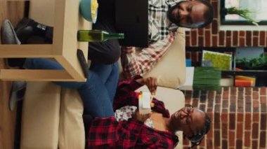 Dikey video: Hayat arkadaşları evde birlikte televizyon izliyor, yemek çubuklarıyla erişte yiyor ve dizüstü bilgisayarlarda internet sitelerine göz atıyorlar. Neşeli, modern çift TV şovuyla eğleniyor, içiyor.