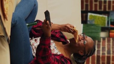 Dikey video: Evde pizza yiyen mutlu kadın, TV 'de bira şişeleri ve fast food siparişleriyle film izlemekten zevk alıyor. Modern bir insan TV 'de izlemekten ve dışarıdan yemek ısmarlamaktan zevk alıyor..