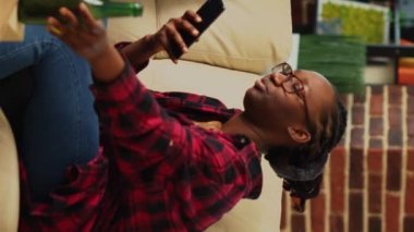 Dikey video: Afro-Amerikan çiftler akıllı telefonlarda internet üzerinden internet kullanarak ve birlikte televizyon izleyerek geziyorlar. Genç modern ortaklar telefon kullanır, yemek ısmarlar..