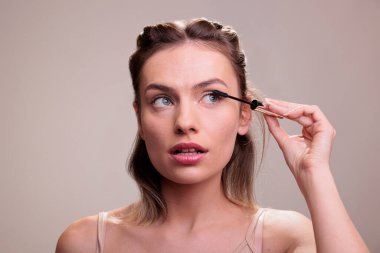 Güzel bir kadın kirpiklerini maskara fırçasıyla fırçalıyor, makyaj yapıyor ve yan tarafa bakıyor. Çekici sarışın manken doğal makyaj rutini ve kirpikleri gösteriyor.