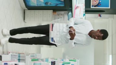 Vertical video: Young customer checking packs of medicine on shelves, looking to buy supplements and healthcare products. Man analyzing medicaments and vitamins from pharmacy shop, retail store.