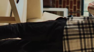 Vertical video: African american guy enjoying pizza from delivery, binge watching favorite tv show in living room. Young happy man eating fast food from takeaway place, sitting at home with action