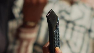 Vertical video: Young girlfriend using tv remote control to watch film with her boyfriend, eating snacks and drinking beer in living room. Modern couple searching for movie on television. Close up.