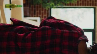 Vertical video: Smiling woman eating pizza and watching tv show, having fun at home with fast food meal delivery and movies. Young adult having dinner and drinking bottle of beer in living room.