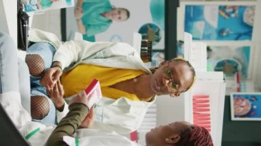 Vertical video: Female specialist explaining drugs treatment in center, talking about prescription medicaments with boxes of pills and vitamins. Clients and pharmacist analyzing pharmaceutics in