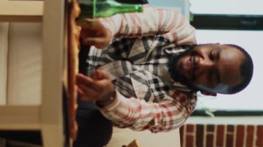Vertical video: Modern people eating pizza at television on sofa, feeling happy binge watching tv show together. Cheerful couple eating fast food takeaway meal in living room, having fun. Handheld