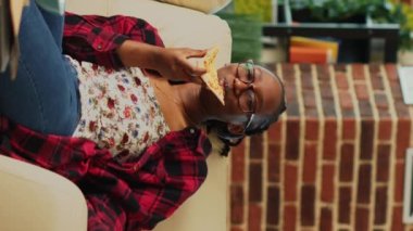 Dikey video: Genç çift pizza yiyorlar ve televizyonda dizi izliyorlar, gülüyorlar ve beraberler. İlişkisi olan bir erkek, en sevdiği filmi izlemek için yemek servisinden zevk alıyor.