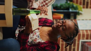 Vertical video: Young couple eating noodles together in living room and binge watching comedy tv series. Life partners feeling happy with asian takeout meal and beer bottles, leisure activity