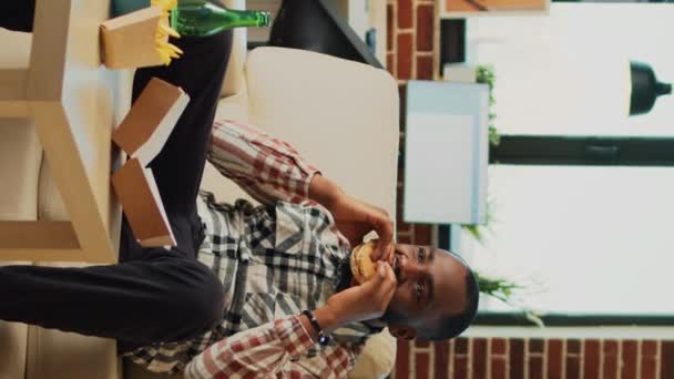 Κάθετη Βίντεο Αφρο Αμερικανός Τρώει Burger Και Πατάτες Στον Καναπέ — Αρχείο Βίντεο