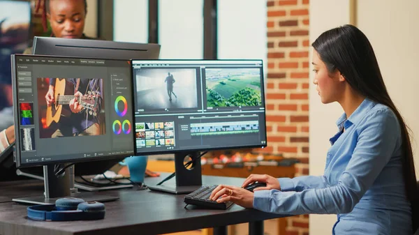 Asian filmmaker editing video and audio footage on multi monitors, creaating movie with professional studio montage. Female videographer using color grading to edit clips in post production agency.