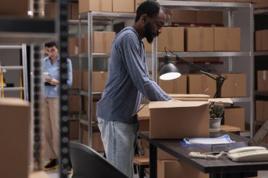 Supervisor putting customer order in cardboard box wrapping with bubble wrap for protection, checking shipping details on laptop computer before delivery package. Worker working in distribution center