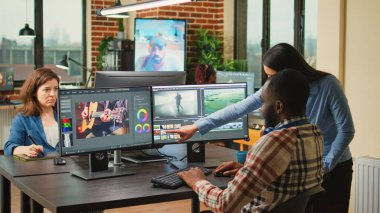 Diverse videographers editing creative film montage on software, brainstorming ideas to improve focus and lighting. Man and woman working with post production video and audio footage.