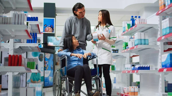 Pharmaceutical worker giving pills box to customer in wheelchair, male caretaker helping person with disabiity. Pharmacist giving medicine pills to client and social worker in drugstore.