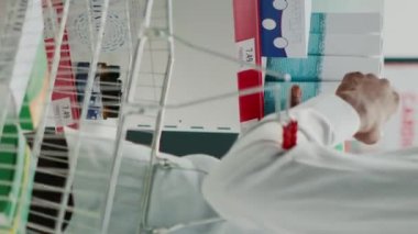 Vertical video: Young man looking at boxes of vitamins in pharmacy, checking pharmaceutical products from shelves. Male client taking medicaments and supplements from racks, pharmaceutics shop.