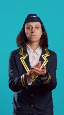Vertical video: Happy woman dressed as stewardess clapping hands, applauding something and feeling positive about commercial flights. Young air hostess doing standing ovation sign and cheering.