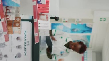 Vertical video: African american woman looking at medicine on racks, buying medicaments and pharmaceutical products from drugstore. Female client taking supplements or vitamins from pharmacy shelves.