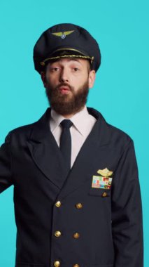 Vertical video: Caucasian man dressed as pilot playing with airplane toy, showing miniature small artificial aircraft on camera. Young adult working as flying captain holding fake mini plane over blue