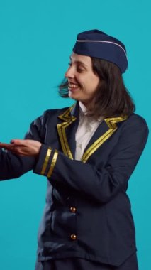 Vertical video: Professional air hostess presenting miniature toy plane, feeling happy about flying occupation. Young woman working as stewardess in uniform showing small artificial airplane on camera