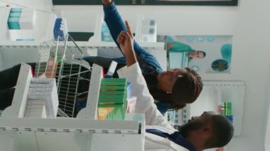 Vertical video: Health specialist helping client with boxes of medicine, giving medical advice to people in pharmacy. Medic talking to customer about treatment and pharmaceutical products. Tripod shot