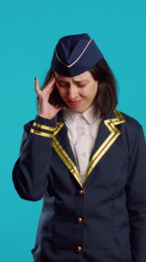 Vertical video: Female airliner dealing with painful migraine, suffering from headache on camera and feeling unhappy. Sick air hostess in uniform suffering from headache, being worried about illness.
