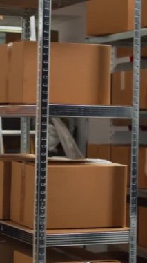 Vertical video: Empty storehouse with office desk and goods to do inventory and ship merchandise to retail clients. Storage room filled with cardboard packages and boxes on storehouse racks, small