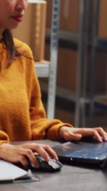 Vertical video: Female entrepreneur checking stock products on pc, using laptop to work on distribution and order management. Woman doing financial planning for business development. Handheld shot.