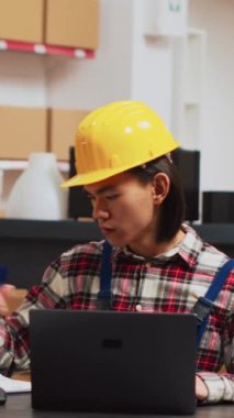 Vertical video: Warehouse employee looking at stock logistics on pc, checking quality of products before planning shipment. Young man working on merchandise products, using laptop for inventory