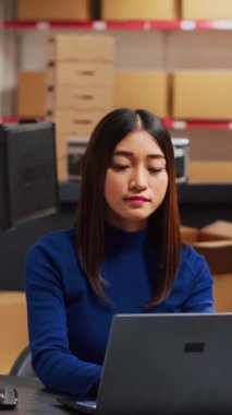 Vertical video: Asian people analyzing merchandise stock in warehouse, looking at quality of retail products in storage room. Entrepreneur and employee working on stock logistics, small business.