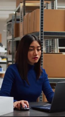 Vertical video: Male worker helping business owner in warehouse, checking stacks of products and retail store supplies. Asian people planning transportation with laptop using stock distribution