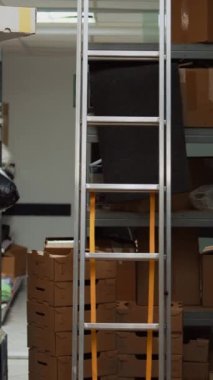 Dikey video: Depoda karton paketlerle dolu küçük işletme deposu, ürün envanteri veya lojistik için dizüstü bilgisayarı olan ofis alanı. Stok için yığınla malı olan boş depo