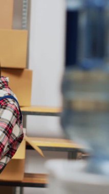 Vertical video: Young man analyzing products in boxes before shipment, checking warehouse stock for distribution on laptop. Depot employee doing quality control, helping with supply chain. Handheld