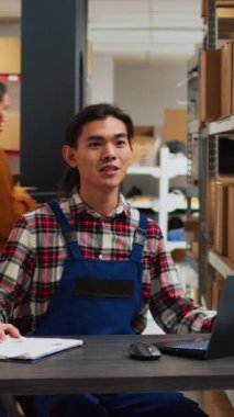 Vertical video: Asian worker recording ad video in storage room, using social media streaming platform to advertise small business in warehouse. Group of people doing teamwork for online promotion.