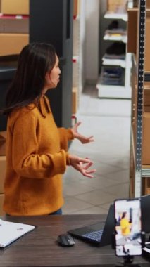 Vertical video: Asian woman doing teleshopping ad for social media promotion, showing merchandise on streaming platform for startup business development. Warehouse owner promoting stock online.