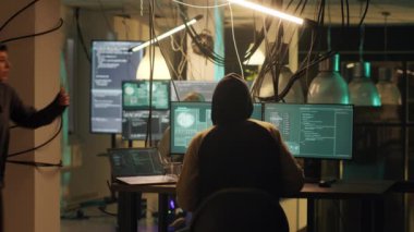 Male criminal planting virus on computer system to access government data with encryption, breaking into server. Thief with anonymous mask doing cryptojacking and theft. Tripod shot.