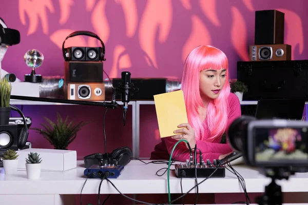 Asian vlogger sitting at desk table in streaming studio recording school supplies review showing notebook at camera., live streaming. Asian creator filming vlog posting content on her channel.