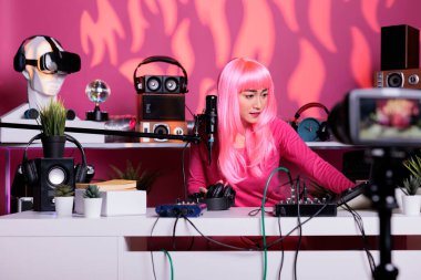 Asian vlogger recording podcast talking with remote subscribers using vlogging microphone standing in streaming studio. Content creator filming lifestyle vlog posting on her channel