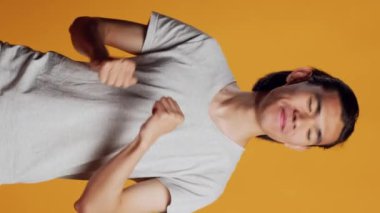 Dikey video: Asyalı adam kamerada havalı dans figürleri gösteriyor, kendine güvenen ve hipster tarzı dans ederek eğleniyor. Dostça ifadeleri olan genç bir model. Havalı davranıyor ve pozitif müzikten hoşlanıyor..