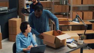 Team of employees working on shipping merchandise to clients, planning retail delivery and shipment. Female adult signing logistics report before sending products in packages, warehouse room.