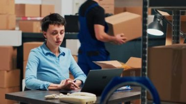 Entrepreneur looking at supplies in boxes before shipping products order to customers, checking distribution and doing quality control. Female employee planning shipment from storehouse.