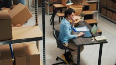 Female entrepreneur analyzing products from warehouse racks, looking at merchandise and boxes before shipping goods order. Young woman working in storage room with supply chain. Tripod shot.