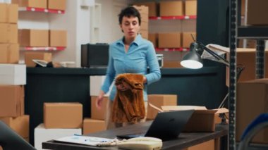 Small business owner putting supplies in cardboard boxes, shipping merchandise to customers. Young woman preparing shipment with warehouse goods, retail and logistics. Tripod shot.