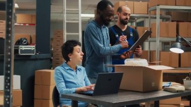 Diverse startup partners doing quality control before shipping goods order, packing merchandise in cardboard boxes. Workers team preparing delivery and shipment in warehouse storage space.