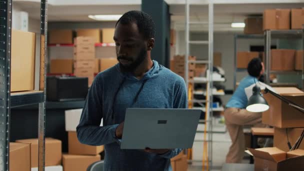 Mężczyzna Pracownik Magazynu Pomocą Laptopa Zapisywania Danych Produktów Analizując Regały — Wideo stockowe