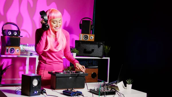 Musician using cutting-edge technology to remix music, listening song using headphones while performing in club at night time. Performer standing at dj table playing with professional mixer