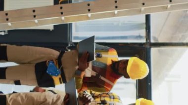 Vertical video: Team of men checking supplies and cargo in depot, using laptop and inventory list in storage room. Workers organizing stock with cardboard boxes on shelves, check merchandise in