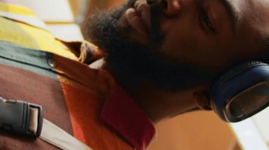 Dikey video: Erkek çalışan müzik dinliyor ve depoda çalışıyor, dans ediyor ve envanter planlamak için tablet kullanıyor. Genç yetişkin kulaklıkla şarkı söylüyor, hisse senedi üretim sevkiyatında çalışıyor.